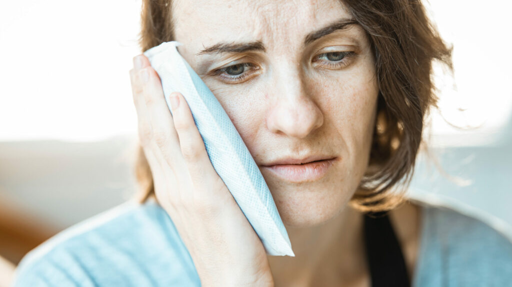 woman looking miserable and holding an ice pack to her cheek